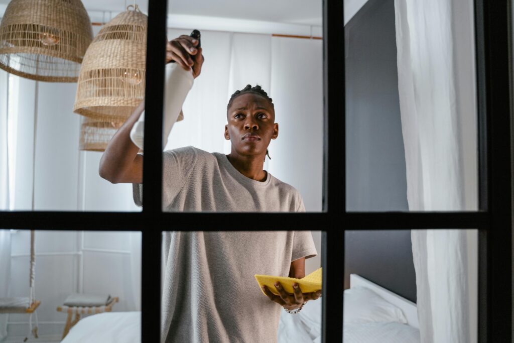 Man cleaning glass window indoors using a spray bottle and cloth.